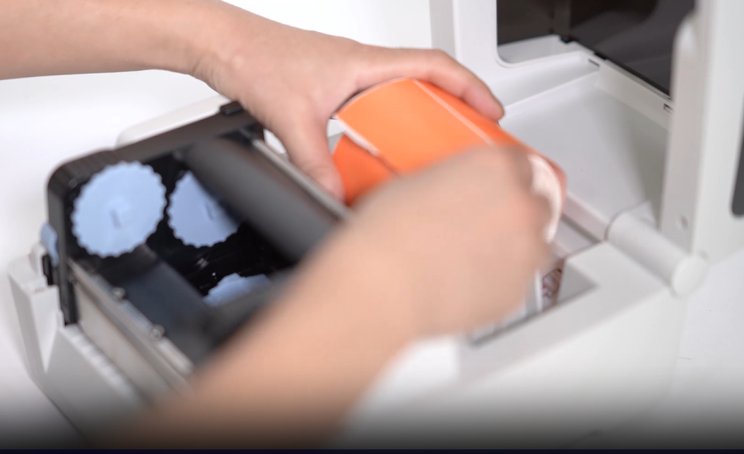 Hands loading a roll of orange labels into a printer.